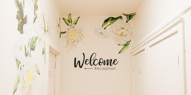 Entrance hallway of Seneca Falls Acupuncture, with floral wall design and large sign that says, "Welcome, Reception."